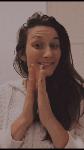 a woman wearing a white sweater is making a funny face with her hands on her face
