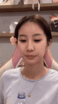 a woman wearing a blue shirt and a necklace is holding a bottle of water in front of her face .