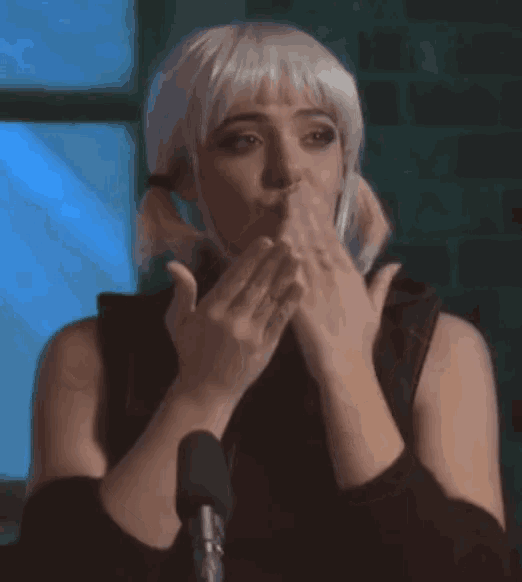 a woman covering her mouth with her hands while wearing a blonde wig