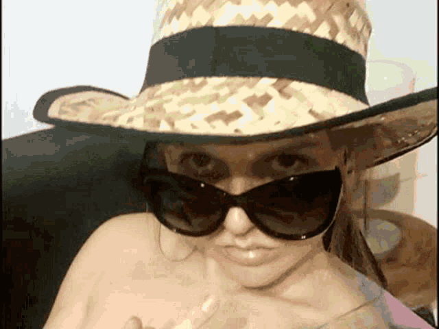 a woman wearing a straw hat and sunglasses holds a glass