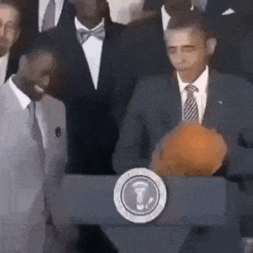 barack obama is holding a basketball in front of a podium .