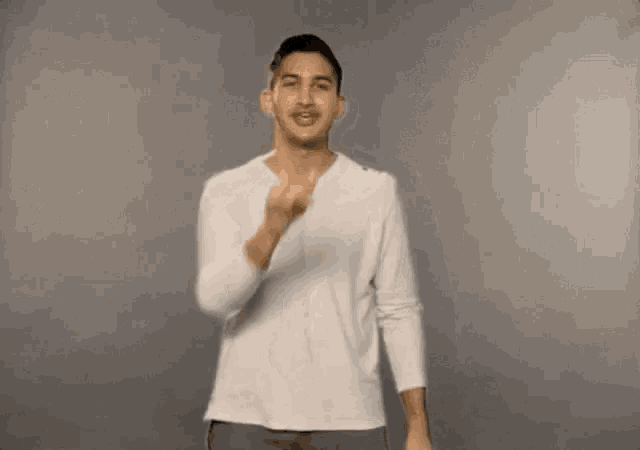 a man in a white shirt and gray pants is making a gesture with his hands .