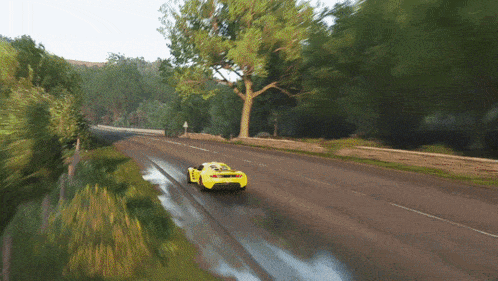 a yellow car is driving down a road with trees in the background