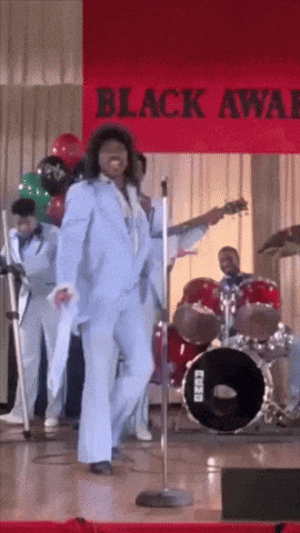 a man in a blue suit sings into a microphone in front of a banner that says black awards