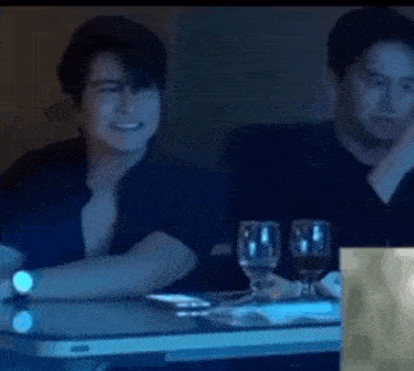 two men are sitting at a table with two glasses of wine .