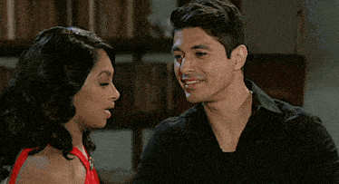 a woman in a red dress smiles while a man looks on