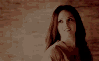 a woman with long red hair is standing in front of a brick wall smiling .