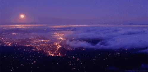 an aerial view of a city at night with a full moon in the background