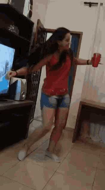 a woman is dancing in a living room with a red cup in her hand