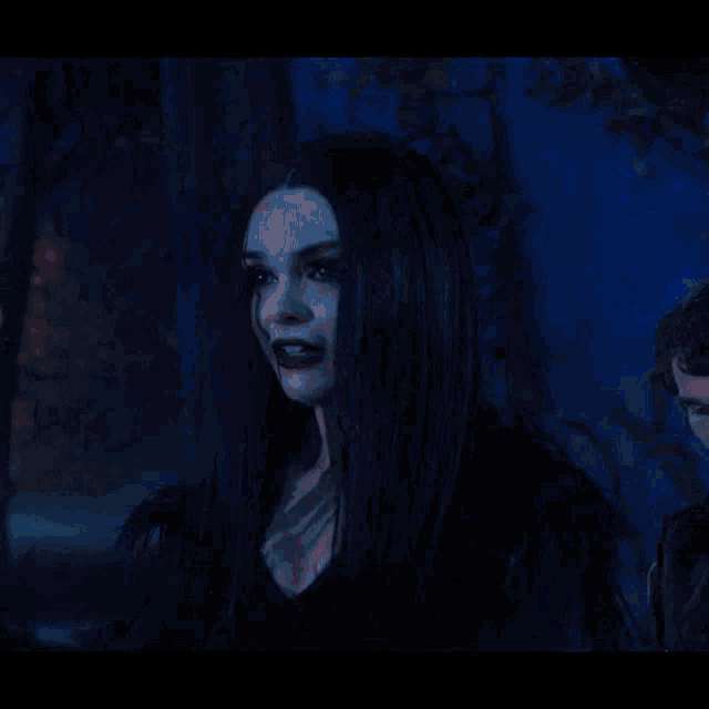 a woman with long black hair and blood on her face is standing next to a man