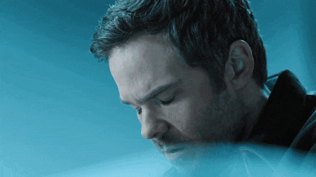 a man with a beard is looking down with a blue background