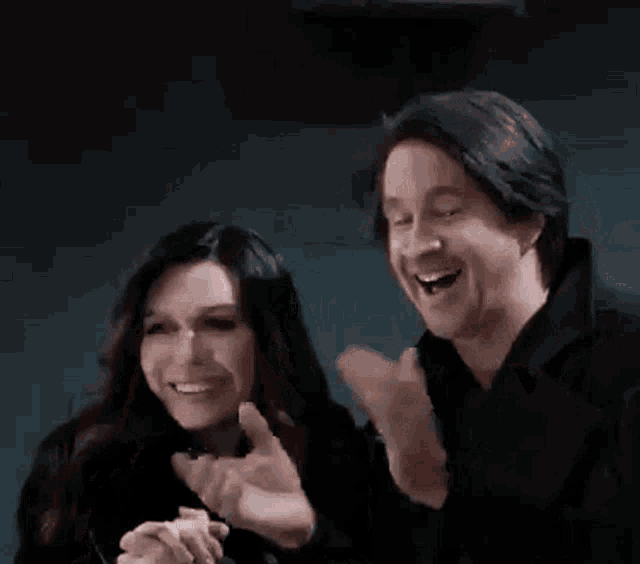 a man and a woman are laughing and clapping their hands .