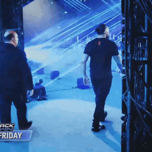 a man in a black shirt walks into a wrestling ring with a sign that says friday