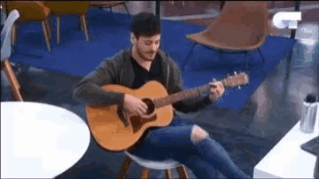 a man is sitting on a chair playing an acoustic guitar in a room .