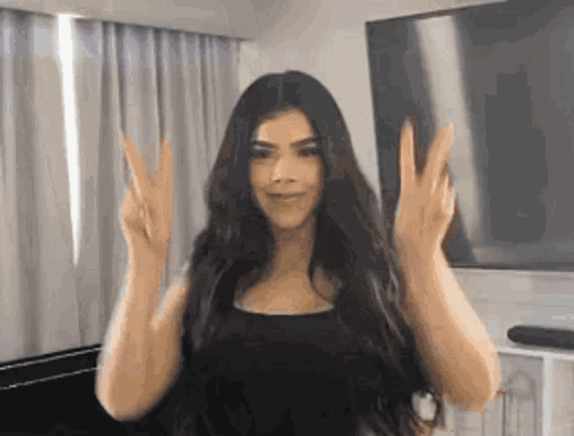 a woman is making a peace sign with her hands in front of a television .