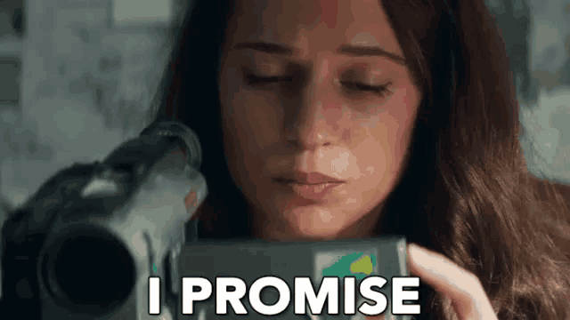 a woman is holding a camera and saying `` i promise '' while looking at it .