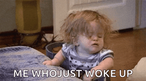 a baby is sitting on a bed with a messy face and the words `` me who just woke up '' written next to it .