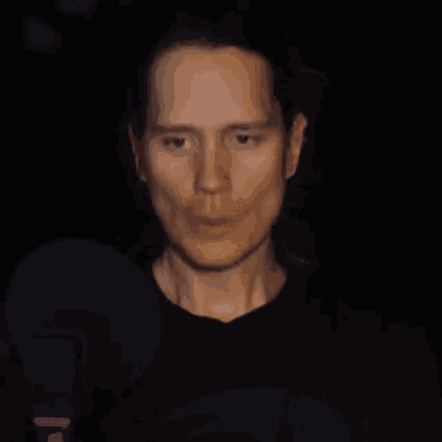 a man with his eyes closed is standing in front of a microphone in a dark room .