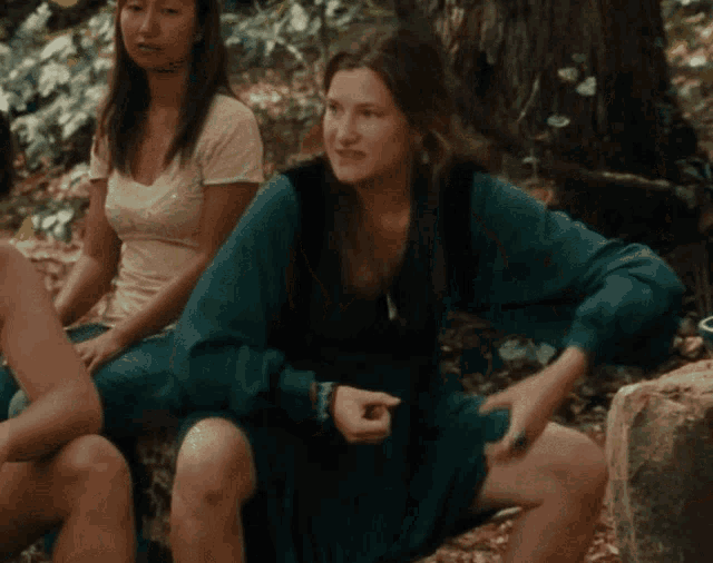 a woman in a blue dress is sitting on a rock in the woods