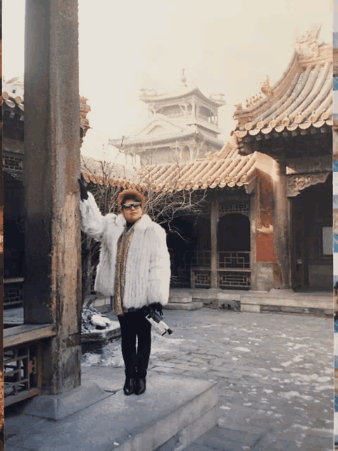 a woman in a fur coat is standing in front of a chinese building