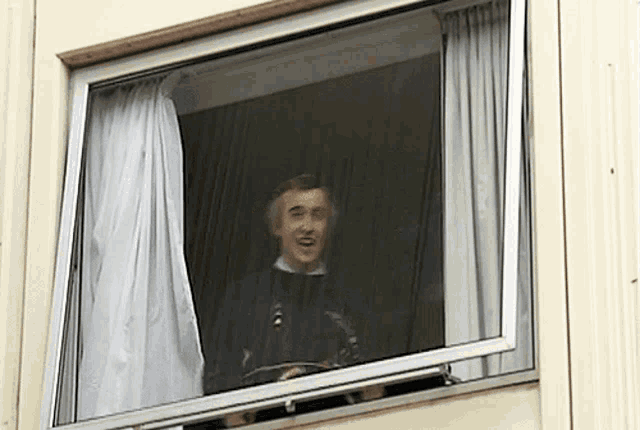 a man is looking out of a window with a white curtain behind him