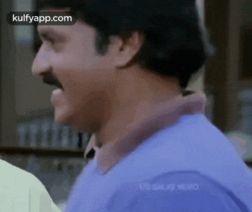 a man with a mustache and a purple shirt is laughing and talking to another man .