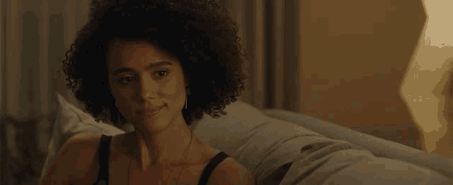 a woman with curly hair sits on a couch in a black tank top