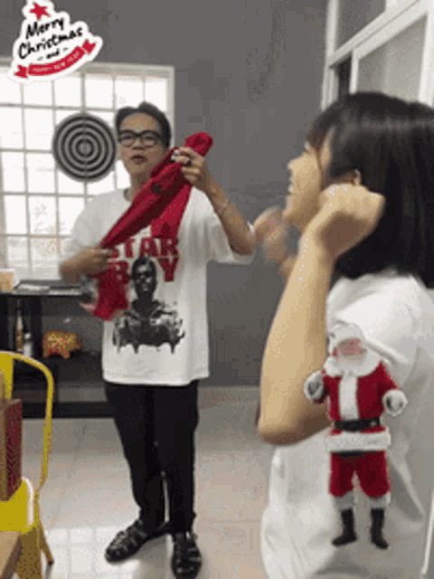 a man wearing a star wars shirt holds a red scarf over a woman