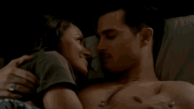 a man and a woman are kissing in bed while the man is shirtless .