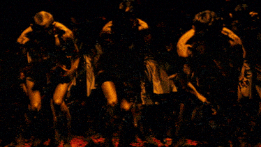 a group of people are sitting in a dark room with their hands on their heads