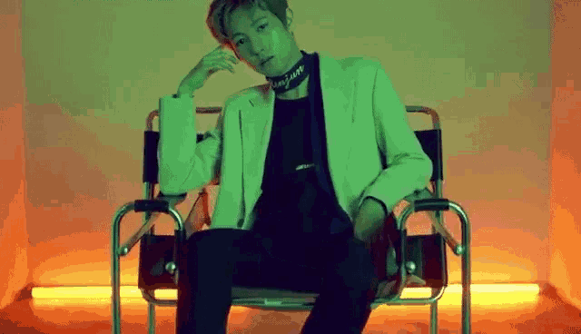 a man in a green jacket is sitting in a chair with his hand on his chin .