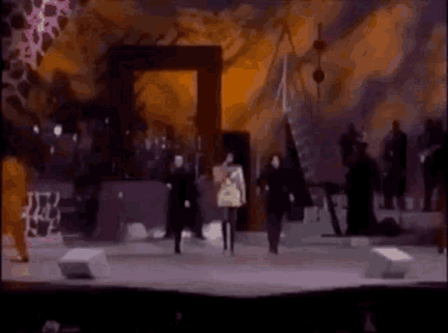 a woman is singing into a microphone on a stage with a group of people dancing behind her .