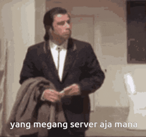 a man in a suit is standing in a room with the words yang megang server aja mana written in the corner