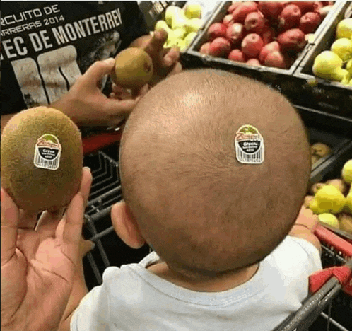 a baby with two kiwi stickers on his head is sitting in a shopping cart