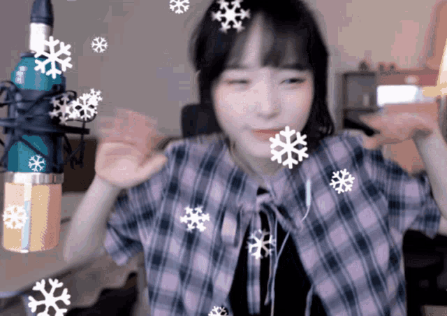 a girl in a plaid shirt is dancing in front of a microphone with snowflakes falling around her