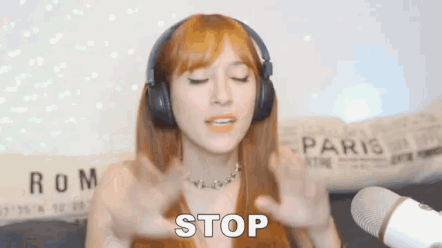a woman wearing headphones and a necklace says stop in front of a microphone