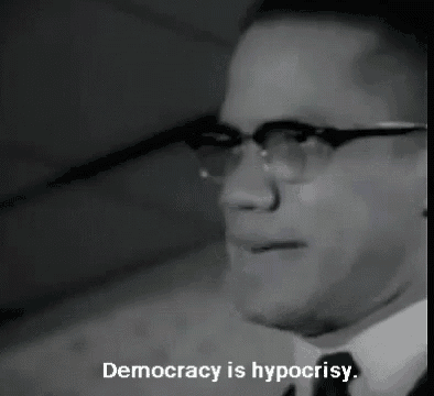 a black and white photo of a man with glasses and the words democracy is hypocrisy