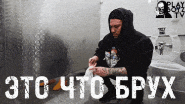 a man in a black hoodie sits in a public restroom with a play boyz logo
