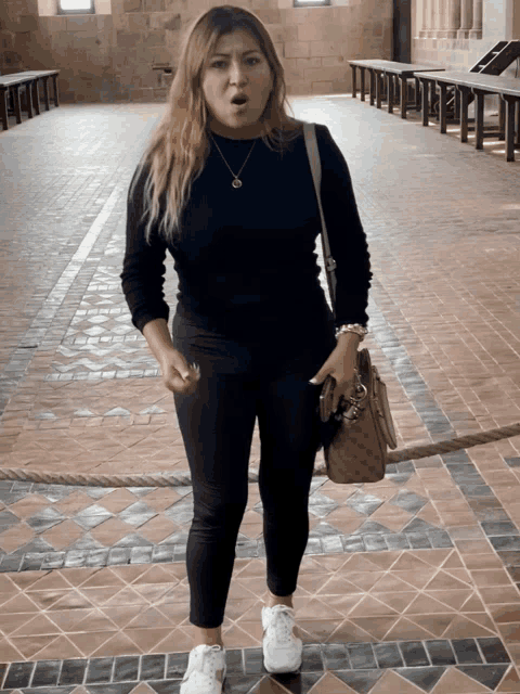 a woman wearing a black sweater and white sneakers is standing in a hallway