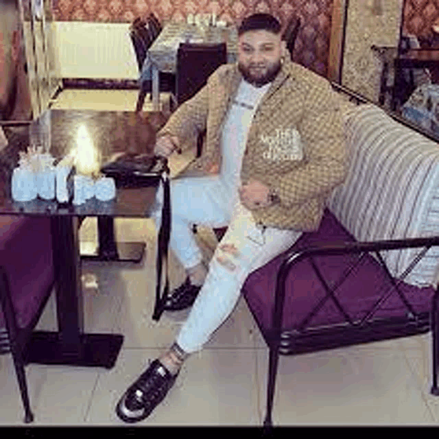 a man is sitting on a couch in a restaurant with a table and chairs .