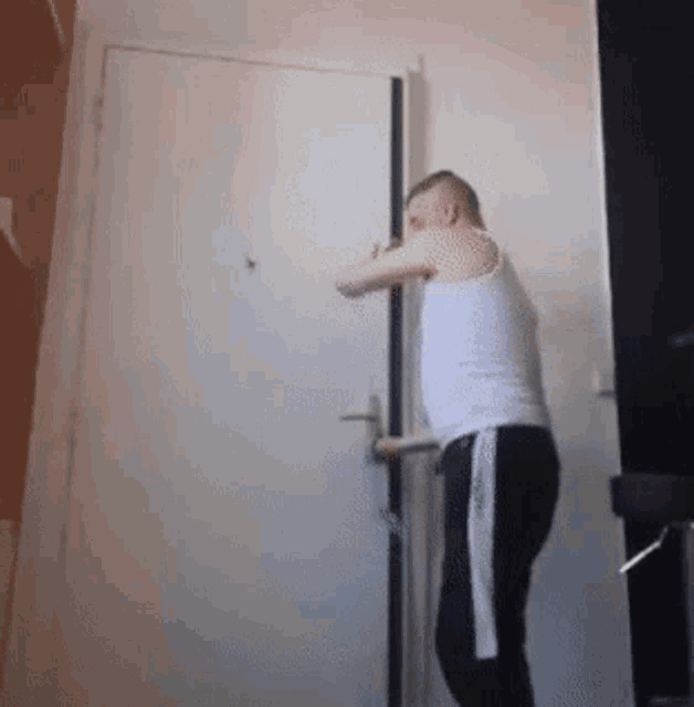 a man in a white tank top and black pants is standing next to a door .