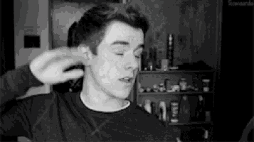 a black and white photo of a young man covering his ear with his hand .