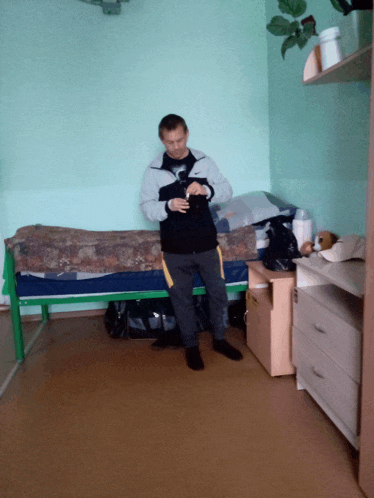 a man sits on a bed in a room with a plant on the shelf