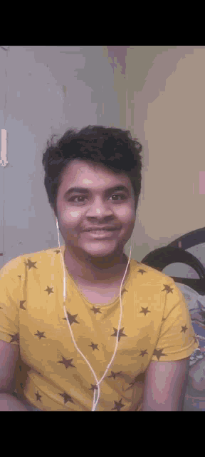 a young man wearing headphones and a yellow shirt with stars on it smiles for the camera .