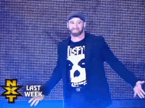 a man in a black jacket and a white shirt is standing in front of a large screen .