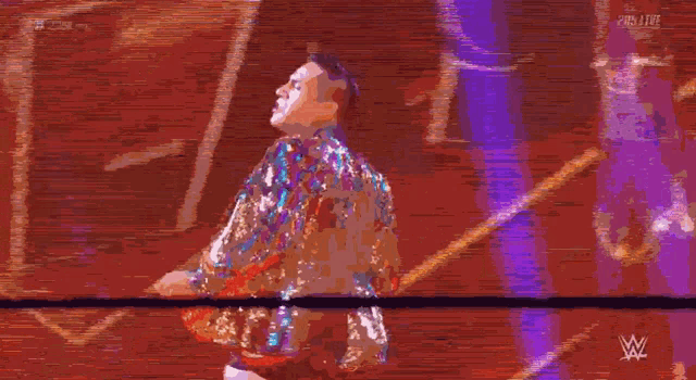 a man in a sequined jacket is standing in a ring with a w logo in the background .