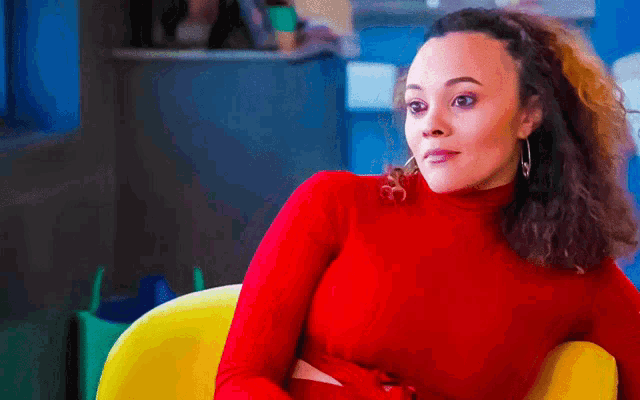 a woman in a red turtleneck is sitting in a yellow chair