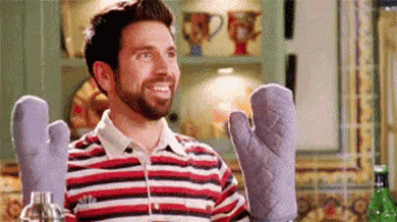 a man with a beard is wearing oven mitts in a kitchen and smiling .