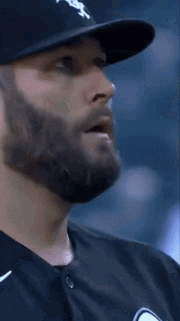 a man with a beard is wearing a white sox hat and a black shirt