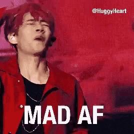 a man in a red jacket is standing on a stage with his mouth open and the words `` mad af '' written on it .